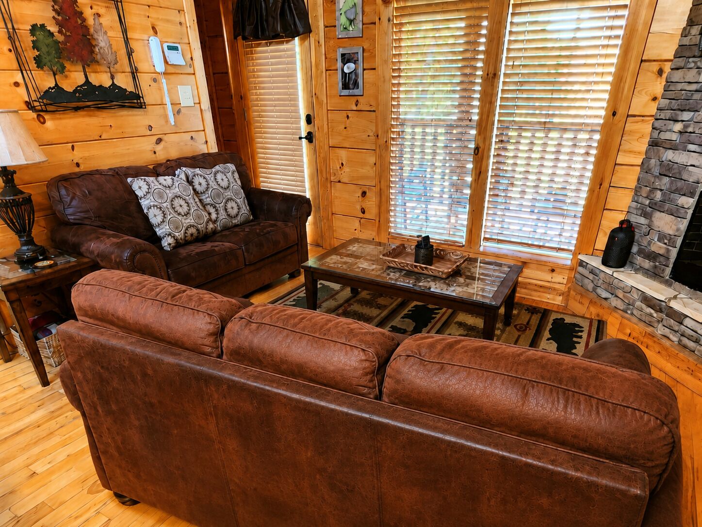 Interior acolhedor de uma cabana de madeira, com um sofá de couro, uma mesa de centro e uma lareira.