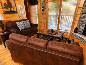 A cozy log cabin interior with a leather sofa, a coffee table, and a fireplace. - Pet-Friendly | Hot Tub | Outdoor TV | Game Room | Views | Sleeps 8 (Sevierville)