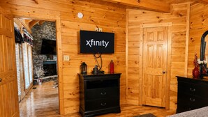 A log cabin interior with a fireplace, wooden walls, a black entertainment unit, and a television mounted on the wall. - Pet-Friendly | Hot Tub | Outdoor TV | Game Room | Views | Sleeps 8 (Sevierville)