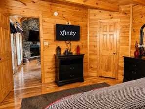 A log cabin interior with a fireplace, wooden walls, a black entertainment unit, and a television mounted on the wall. - Pet-Friendly | Hot Tub | Outdoor TV | Game Room | Views | Sleeps 8 (Sevierville)