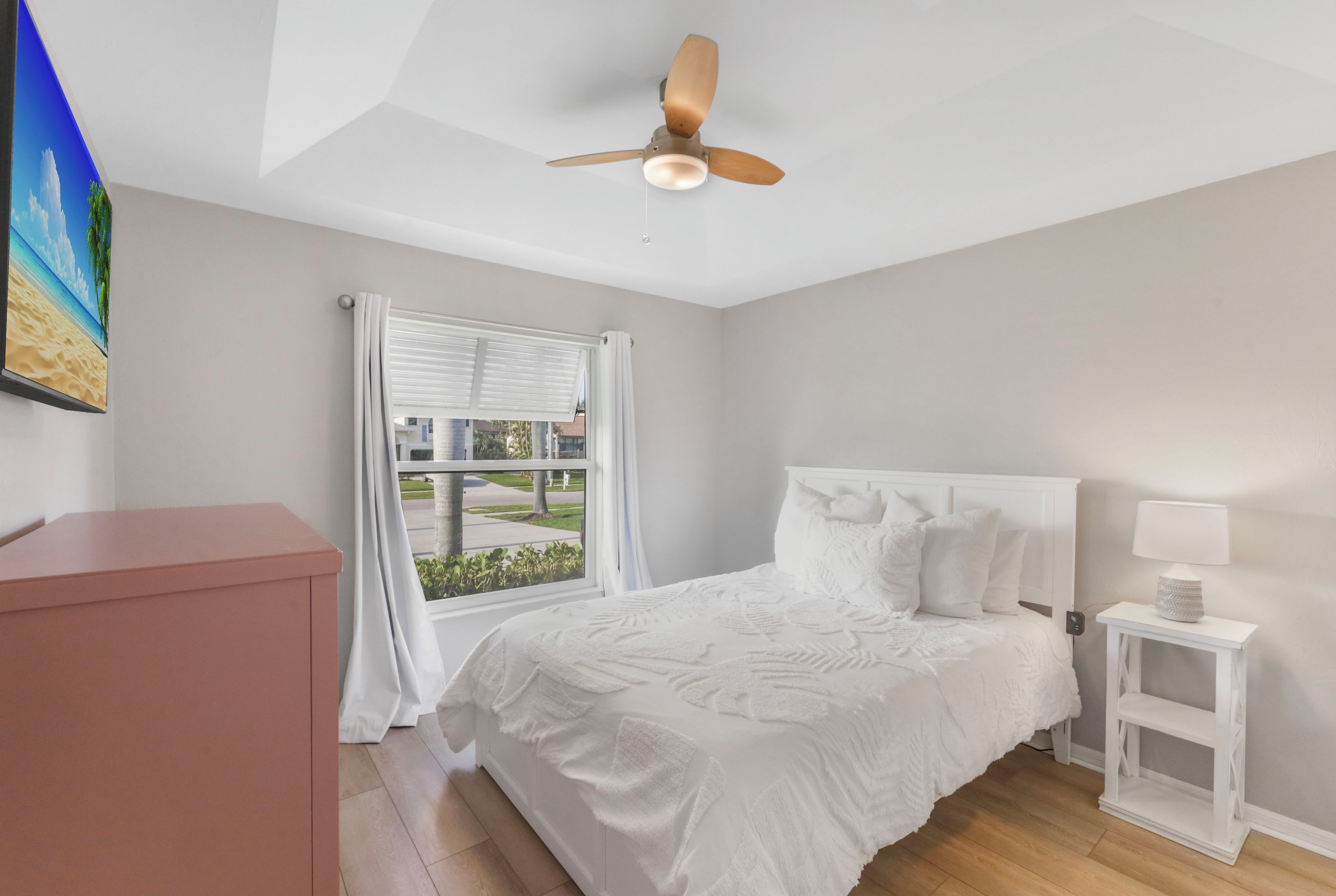 Ein Schlafzimmer mit Bett, Deckenventilator, Fenster mit Vorhängen, Nachttisch und einem rosa Schrank.