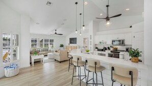 Una cocina amplia con armarios blancos, una isla central con taburetes de bar y un ventilador de techo.