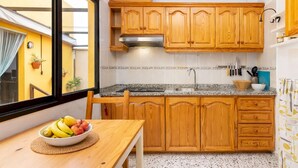 Eine kleine Küche mit Holzschränken, einer Arbeitsplatte aus Granit und einer Obstschale auf dem Tisch.