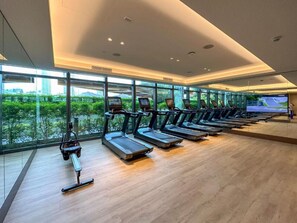 A gym with treadmills, a rowing machine, and a TV screen. - Elegant 2BR Opera Apartment | Balcony • Pool Access • Free Parking (Dubai)