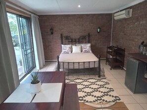 Una camera da letto con un letto, una scrivania, una sedia, una pianta in vaso, un tappeto decorato e un muro in mattoni.