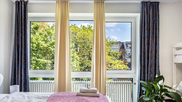 A bedroom with a bed, a window with curtains, a radiator, and a potted plant. - St. Pauli Urban Hideaway – Modern Apartment with Playground, Near Beach and Transport (Hamburg)