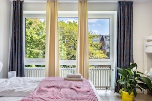 A bedroom with a bed, a window with curtains, a radiator, and a potted plant. - St. Pauli Urban Hideaway – Modern Apartment with Playground, Near Beach and Transport (Hamburg)