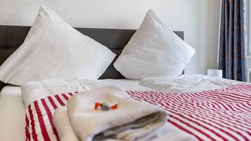 Een net opgemaakt bed met witte kussens, een gestreepte rode en witte dekbedovertrek, en een opgevouwen handdoek op het bed.