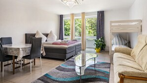 A modern room with a bed, sofa, dining table, chairs, and a balcony with curtains. - St. Pauli Urban Hideaway – Modern Apartment with Playground, Near Beach and Transport (Hamburg)