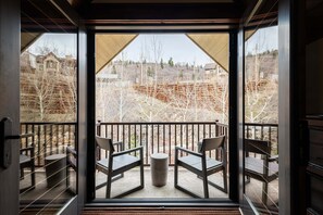 Ein Balkon mit zwei Stühlen und einem kleinen Tisch, mit Blick auf eine Baustelle mit kahl stehenden Bäumen und Gebäuden.