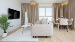 Ett modernt vardagsrum med en soffa, ett matbord, stolar, en tv och en krukväxt.