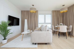A modern living room with a sofa, dining table, chairs, a TV, and a potted plant. - Elegant Apartment | Parking, Balcony, Air Conditioning (Warszawa)