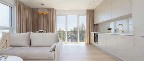 A modern apartment with a sofa, a dining table, a kitchen with white cabinets, and a balcony with curtains.