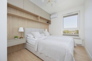 A bedroom with a bed, bedside tables, a window, and built-in shelving. - Elegant Apartment | Parking, Balcony, Air Conditioning (Warszawa)