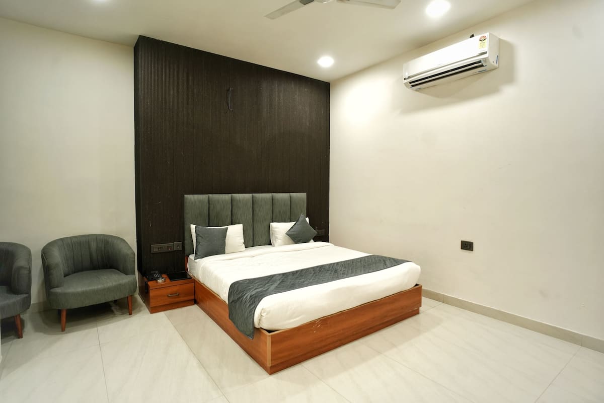 Un dormitorio moderno con estructura de cama de madera, cabecera oscura, sofá gris y aire acondicionado de pared.