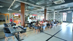 A modern indoor dining area with multiple tables and chairs, a visible food counter, and a large pillar. - HOTEL HIGHWAY QUEEN (Dudu)