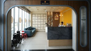 A reception area with a reception desk, a blue sofa, a wheelchair, and a wall with framed pictures. - HOTEL HIGHWAY QUEEN (Dudu)