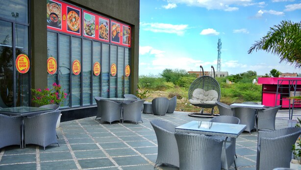 An outdoor patio with wicker furniture, a glass table, and a building with food menu posters. - HOTEL HIGHWAY QUEEN (Dudu)