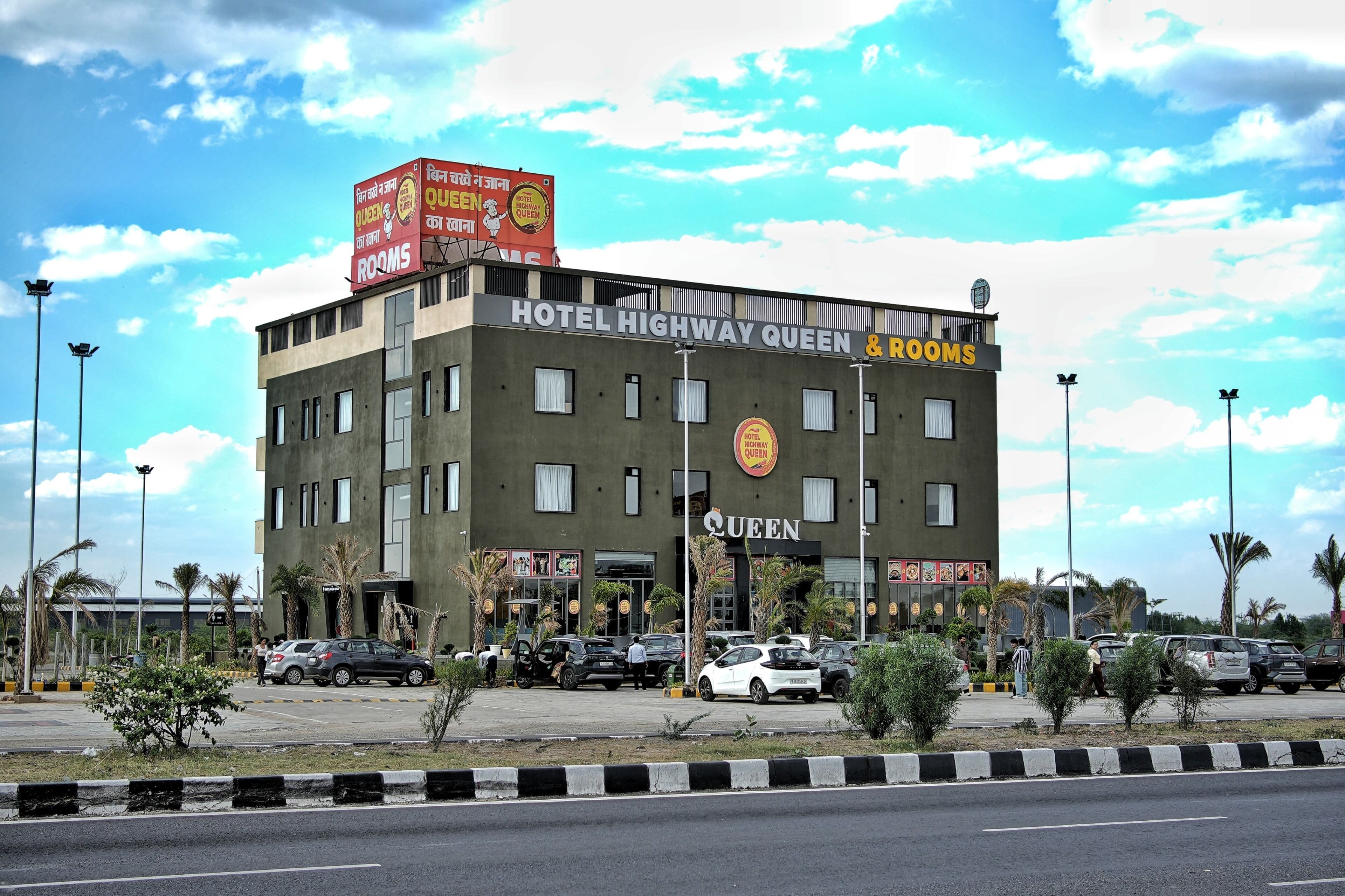 Un hotel con un letrero que dice 'HOTEL HIGHWAY QUEEN & ROOMS' y un gran cartel publicitario encima.