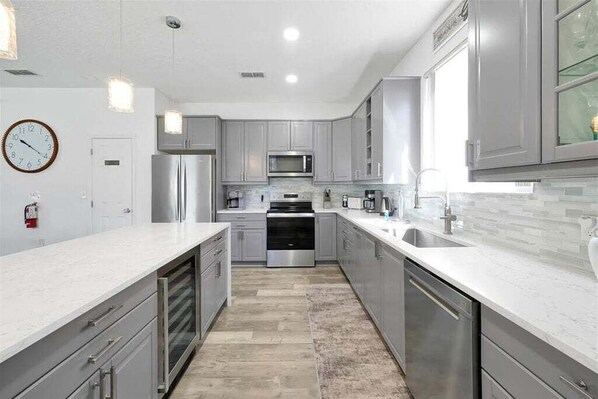 A modern kitchen with stainless steel appliances, white cabinetry, and a marble countertop. - 6BR Oasis w/ Private Pool, Game Room & Lanai (Davenport)