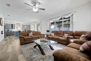 A spacious living room with a glass coffee table, two sofas, and a ceiling fan. - 6BR Oasis w/ Private Pool, Game Room & Lanai (Davenport)