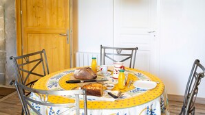 Een eettafel met een gele tafelkleed, een brood, een mes, een kom en een fles sinaasappelsap.