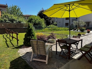 Une terrasse agrémentée d’un parasol jaune, de mobilier d’extérieur et d’un jardin bien entretenu.