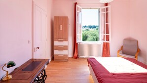 Een slaapkamer met een bed, een bureau, een stoel, een kledingkast en een raam met gordijnen.