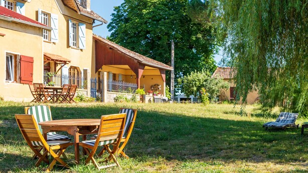 Een huis met een terras, tuinmeubilair en een grote boom.