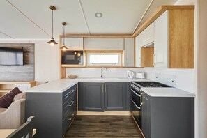 A compact kitchen with a microwave, stove, and sink, wooden cabinetry, and pendant lighting. - Host & Stay | Tommy's Lodge (Felton)