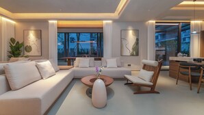 Una sala de estar moderna con sofá, mesa de centro y sillas, un comedor con mesa y sillas, y ventanas grandes con vistas.
