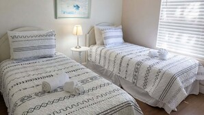Two beds with patterned bedding, a bedside lamp, a framed picture on the wall, and a window with blinds. - Family 3BR Near Disney | Pool & Fenced Yard (Kissimmee)