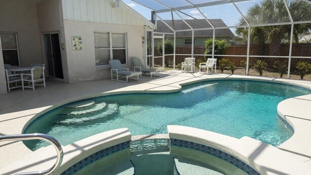 A swimming pool with a glass enclosure, surrounded by lounge chairs and a covered patio area. - Family 3BR Near Disney | Pool & Fenced Yard (Kissimmee)