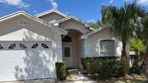 A residential house with a garage, a front door, and a small garden with a palm tree. - Family 3BR Near Disney | Pool & Fenced Yard (Kissimmee)