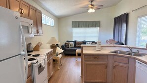 A compact kitchen with a microwave, stove, sink, and wooden cabinets. - Family 3BR Near Disney | Pool & Fenced Yard (Kissimmee)