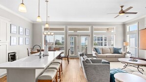 Een ruime keuken met een centraal kookeiland, een eethoek met tafel en stoelen, een bank en een plafondventilator.