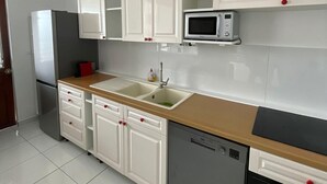 Une cuisine avec des meubles blancs, un four à micro-ondes, un évier, un réfrigérateur et un lave-vaisselle.