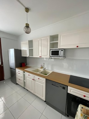 A kitchen with white cabinets, a microwave, a sink, a refrigerator, and a dishwasher. - Your home in Fort de France (Fort-de-France)