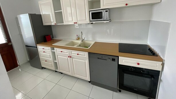 Une cuisine avec des meubles blancs, un four à micro-ondes, un évier, un lave-vaisselle et une cuisinière.