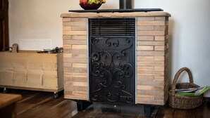 Une cheminée en briques agrémentée d’une grille décorative en métal, un banc en bois et un panier en osier.