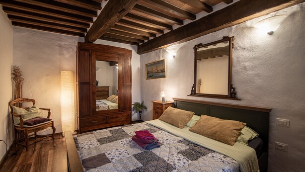 Une chambre avec un plafond en bois, un lit recouvert d’une courtepointe, une chaise, une table de chevet et un miroir.