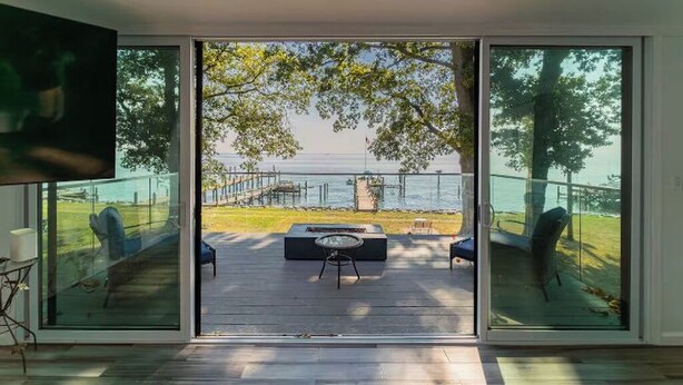 Ein modernes Interieur mit einer großen Schiebeglasdoor, die auf eine Terrasse mit Meerblick und einem Steg führt.