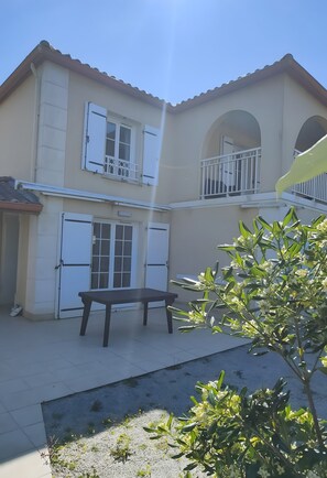 A two-story building with a balcony, a table, and a small garden area. - Holiday Home for 6, 100 m from the Sea, Sea View, Shared Pool! (Bretignolles-sur-Mer)