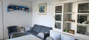 Et værelse med en grå sofa, et hvidt bord, en blå reol med bøger, et billede i ramme på væggen og et skab med service.