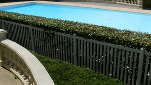 Una piscina con una valla blanca y setos, rodeada de edificios residenciales.