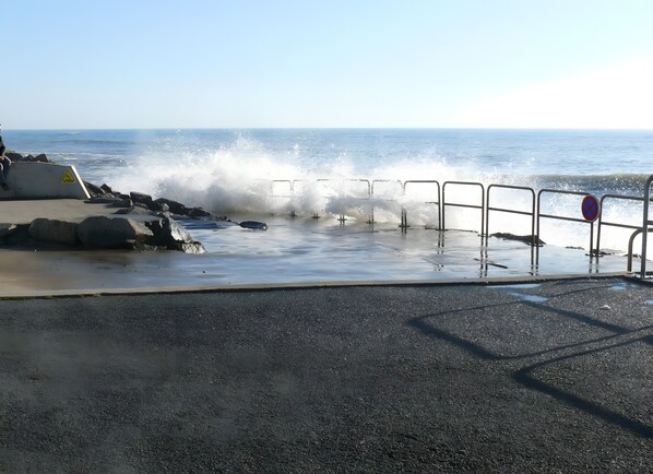 A coastal walkway with a railing, a warning sign, and a no-entry sign.