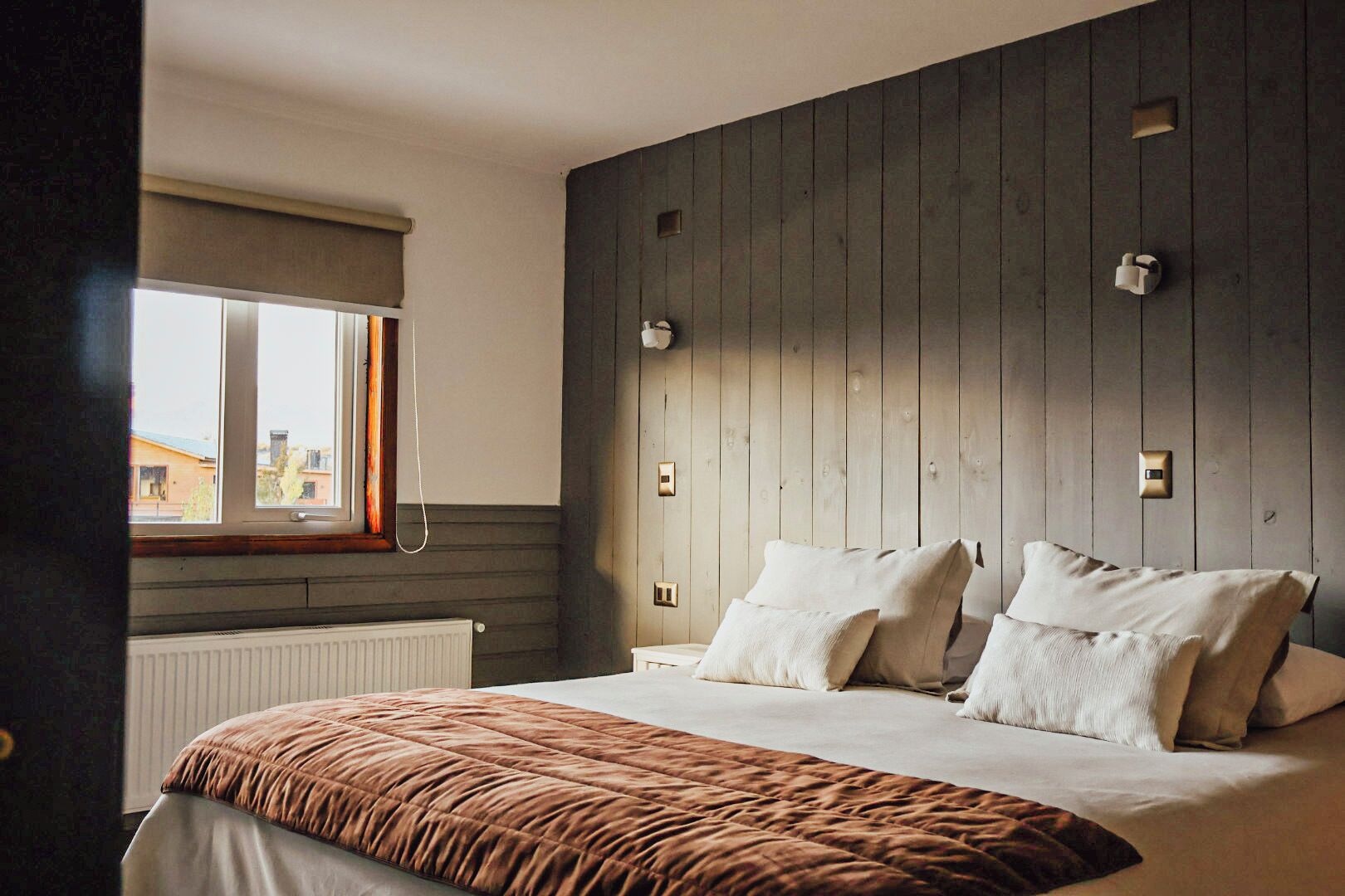 A bedroom with a large bed, a window with a view, and wooden paneling on the wall.