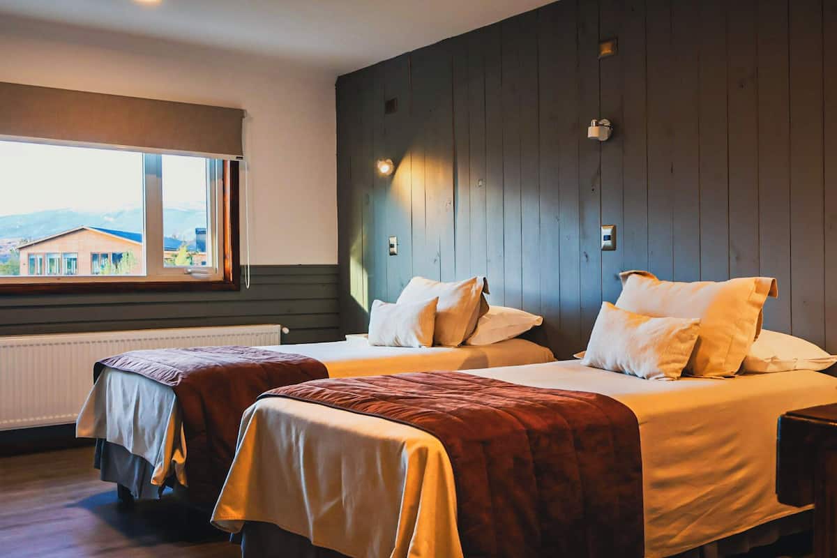 Quarto com duas camas, janela com vista e parede de madeira.