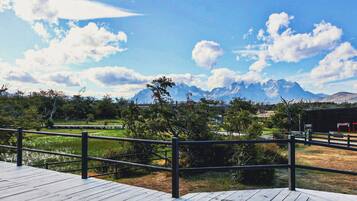A wooden deck with a metal railing, a grassy area, and a mountain range in the background.