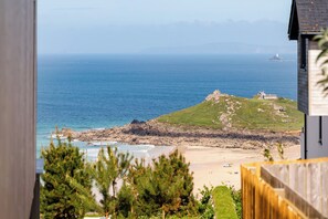 A coastal view with a beach, rocky terrain, and a lighthouse in the distance. - Hidden 9- Grand Bay Suite Hot Tub (St Ives)